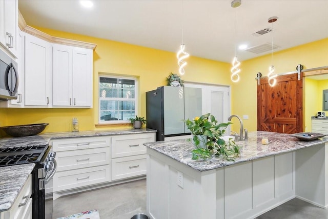 kitchen with a barn door, hanging light fixtures, an island with sink, stainless steel appliances, and white cabinets