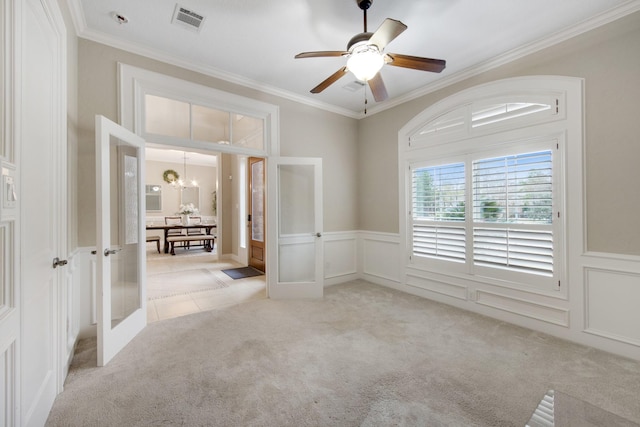 carpeted spare room with crown molding, ceiling fan with notable chandelier, and french doors