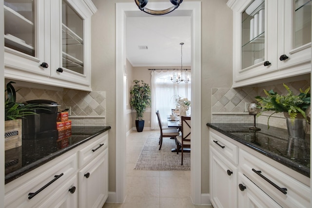 bar with white cabinetry, tasteful backsplash, a notable chandelier, light tile patterned flooring, and dark stone countertops