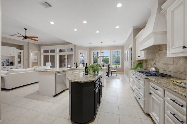 kitchen featuring stainless steel appliances, decorative backsplash, hanging light fixtures, a center island with sink, and custom range hood