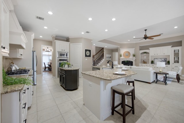 kitchen with ceiling fan, a breakfast bar, white cabinetry, light stone countertops, and a large island