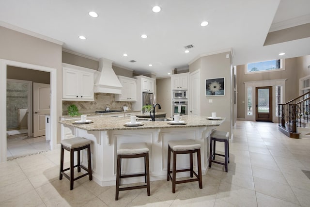 kitchen with custom exhaust hood, a kitchen bar, white cabinetry, sink, and a large island