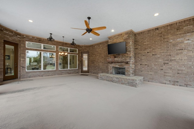 unfurnished living room with carpet floors, ceiling fan with notable chandelier, brick wall, and a stone fireplace