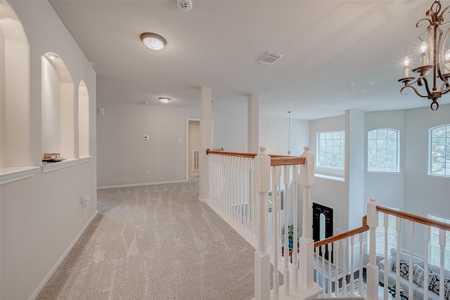 hall with an inviting chandelier and light carpet