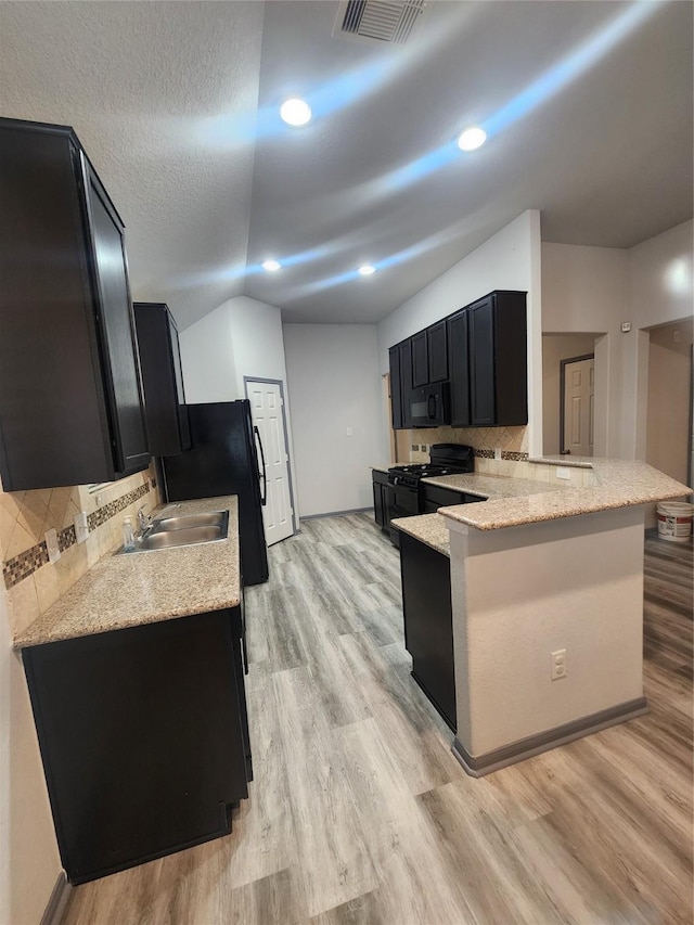 kitchen with kitchen peninsula, tasteful backsplash, sink, black appliances, and light wood-type flooring