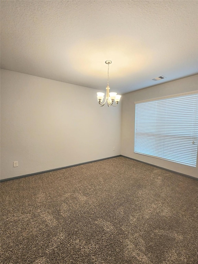 spare room featuring carpet floors, a textured ceiling, and an inviting chandelier