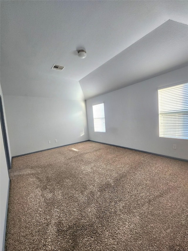 carpeted spare room featuring vaulted ceiling and a textured ceiling