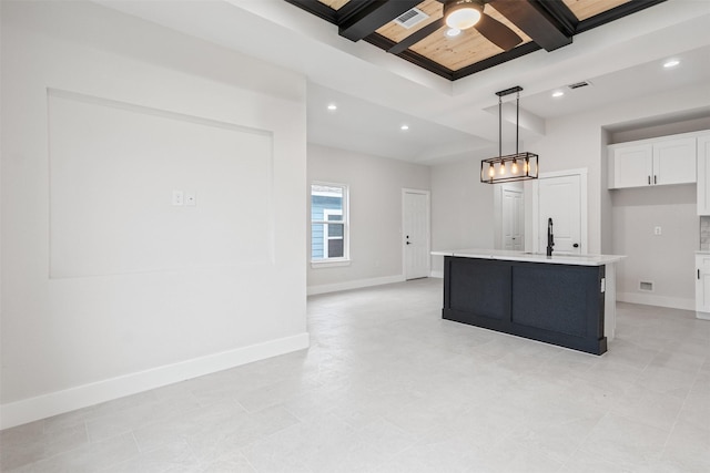 kitchen featuring hanging light fixtures, an island with sink, beamed ceiling, ceiling fan, and white cabinetry