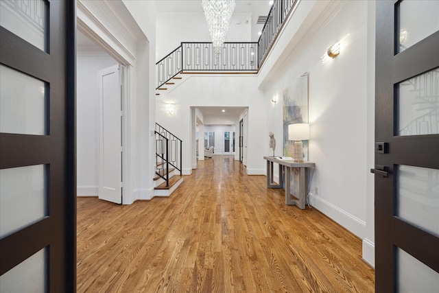 foyer with crown molding, light wood-type flooring, an inviting chandelier, and a towering ceiling