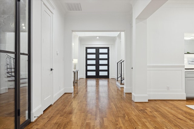 foyer entrance with light hardwood / wood-style flooring, french doors, and crown molding