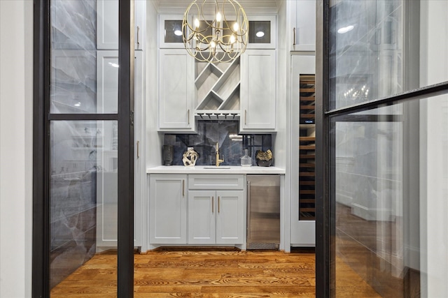 bar with wood-type flooring, stainless steel refrigerator, pendant lighting, white cabinets, and an inviting chandelier