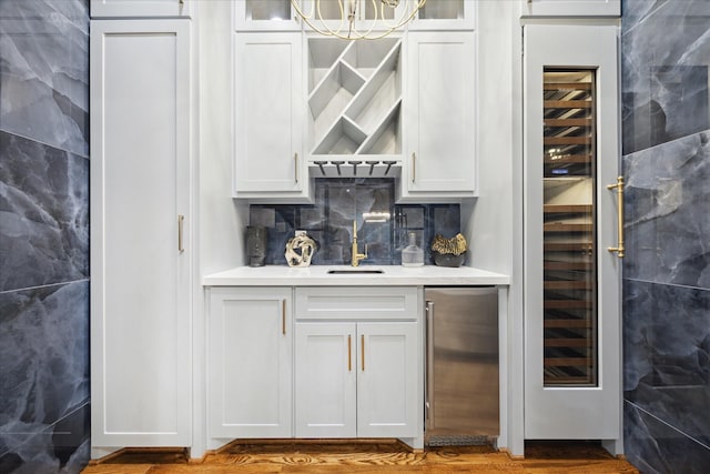 bar with sink, white cabinetry, tile walls, stainless steel refrigerator, and wine cooler