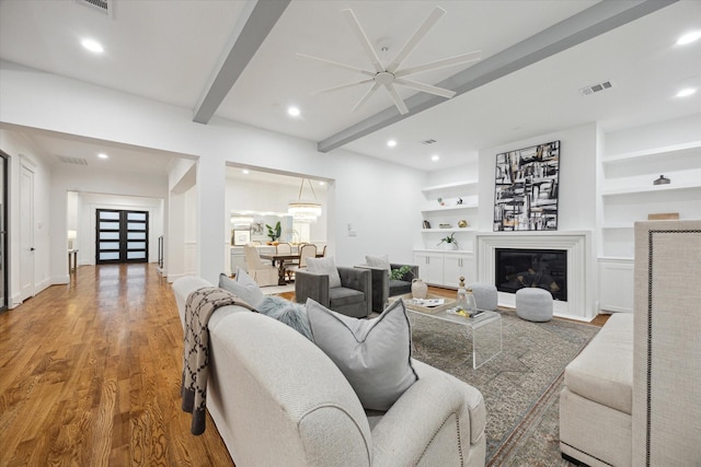 living room featuring wood-type flooring, ceiling fan, built in shelves, and beamed ceiling