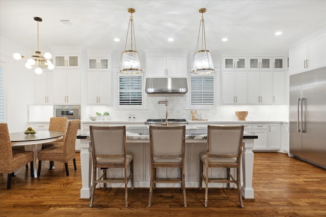 kitchen featuring an island with sink, appliances with stainless steel finishes, hanging light fixtures, and white cabinetry