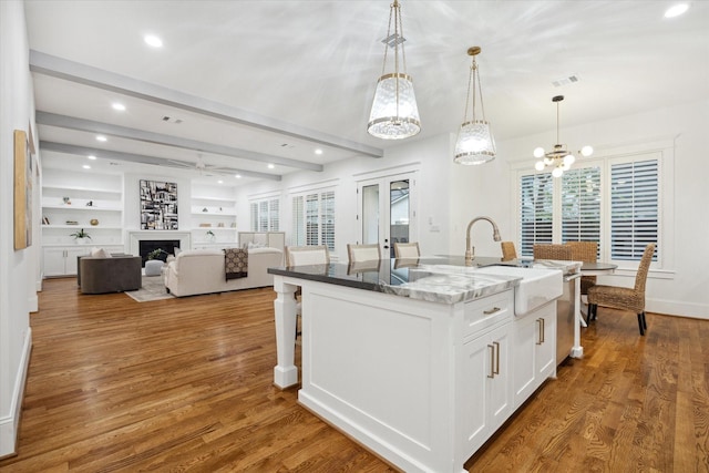 kitchen featuring light stone countertops, hanging light fixtures, a center island with sink, white cabinetry, and beamed ceiling