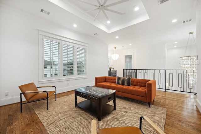 living room featuring ceiling fan with notable chandelier, a raised ceiling, ornamental molding, and hardwood / wood-style floors