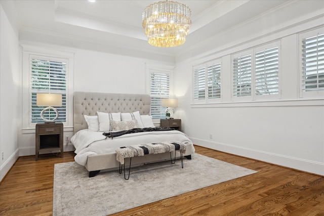 bedroom with hardwood / wood-style floors, crown molding, a chandelier, and a tray ceiling