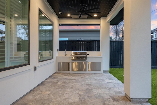 patio terrace at dusk featuring ceiling fan, area for grilling, and an outdoor kitchen