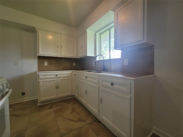 kitchen with white range, dark tile patterned floors, decorative backsplash, sink, and white cabinetry