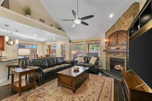 living room with a stone fireplace, crown molding, ceiling fan, dark wood-type flooring, and sink