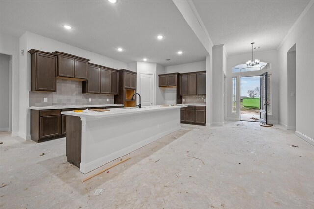 kitchen with sink, a center island with sink, tasteful backsplash, an inviting chandelier, and dark brown cabinetry