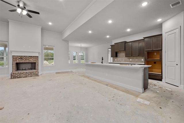 kitchen featuring decorative backsplash, a kitchen island with sink, a fireplace, ceiling fan, and sink