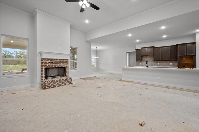 unfurnished living room with sink, a brick fireplace, a wealth of natural light, and ceiling fan with notable chandelier