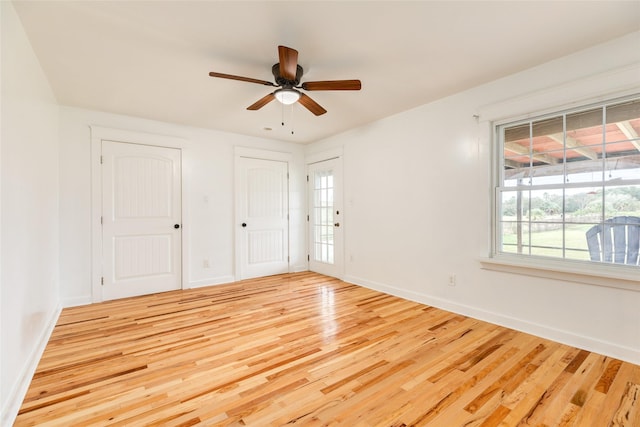 unfurnished bedroom featuring ceiling fan, light wood-type flooring, and multiple closets