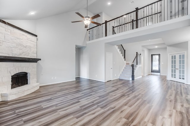 unfurnished living room featuring high vaulted ceiling, ceiling fan, light hardwood / wood-style flooring, and a stone fireplace