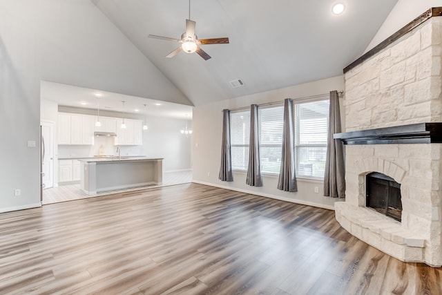 unfurnished living room with sink, ceiling fan, light hardwood / wood-style floors, high vaulted ceiling, and a stone fireplace