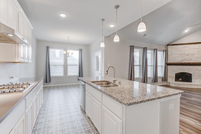 kitchen with sink, a kitchen island with sink, white cabinetry, appliances with stainless steel finishes, and a stone fireplace