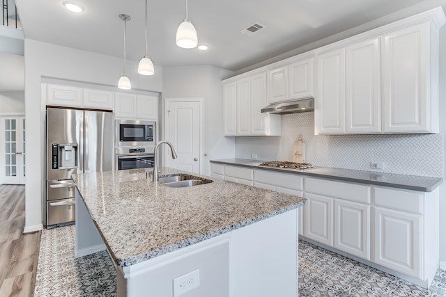 kitchen featuring white cabinets, stainless steel appliances, an island with sink, light stone counters, and sink