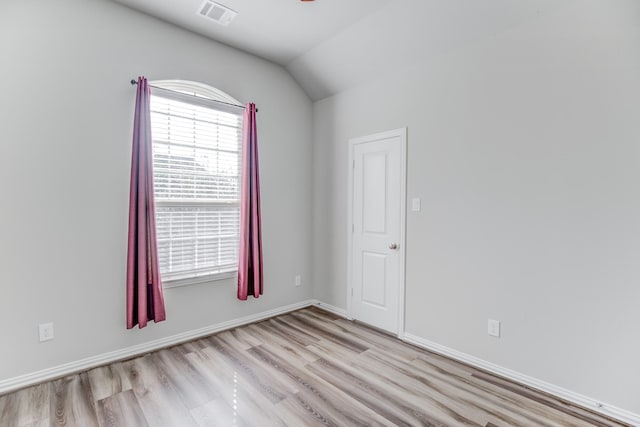 spare room featuring light wood-type flooring and vaulted ceiling