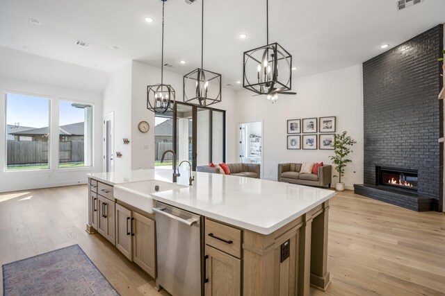 kitchen featuring a brick fireplace, stainless steel dishwasher, a kitchen island with sink, and sink