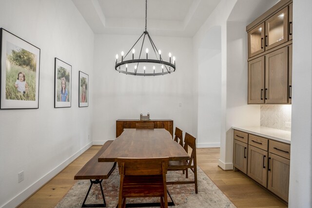 dining area featuring light wood-type flooring, a notable chandelier, and a tray ceiling