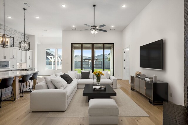 living room with ceiling fan with notable chandelier and light hardwood / wood-style floors