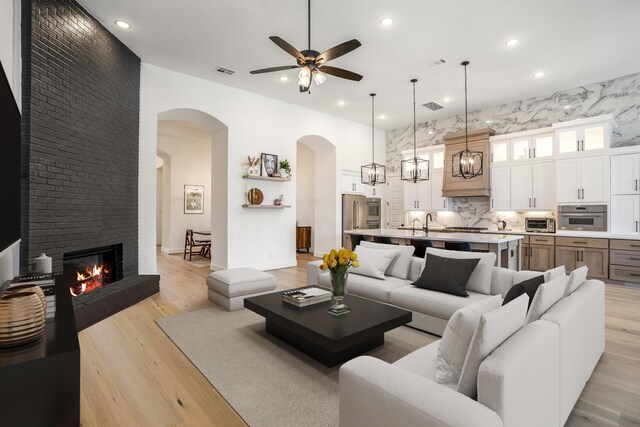 living room featuring a large fireplace, light wood-type flooring, ceiling fan, and sink