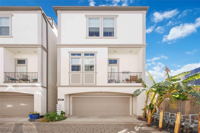 view of front of house featuring a balcony, an attached garage, decorative driveway, and stucco siding