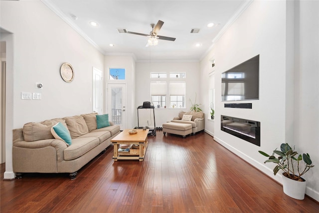 living room featuring dark wood finished floors, a glass covered fireplace, visible vents, and crown molding