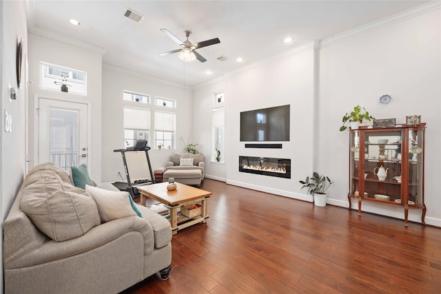 living room with baseboards, visible vents, a glass covered fireplace, ornamental molding, and dark wood-style flooring