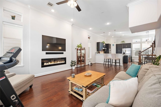 living room featuring visible vents, stairs, ornamental molding, dark wood-style floors, and a glass covered fireplace