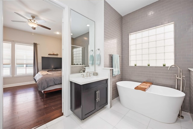 ensuite bathroom featuring a soaking tub, ensuite bath, ceiling fan, tile patterned floors, and tile walls