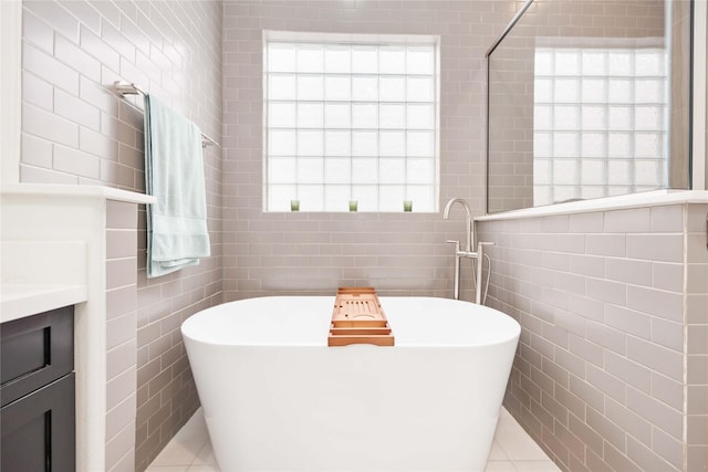 full bath with a healthy amount of sunlight, tile walls, a freestanding bath, and vanity