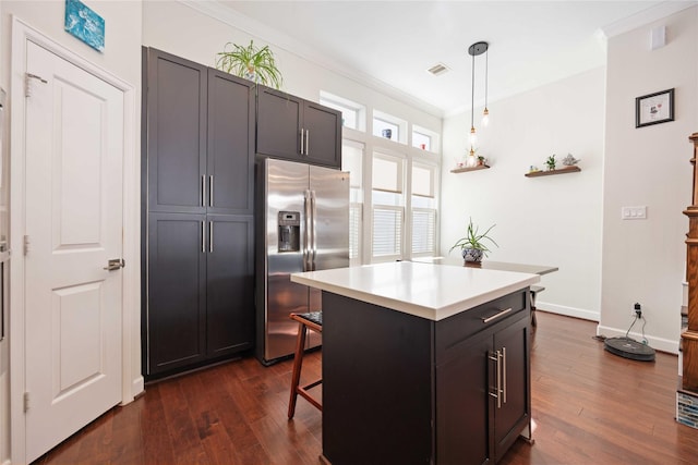 kitchen with stainless steel fridge, a breakfast bar area, a center island, decorative light fixtures, and light countertops