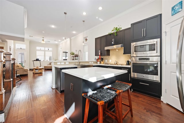 kitchen with appliances with stainless steel finishes, a breakfast bar, open floor plan, light countertops, and under cabinet range hood