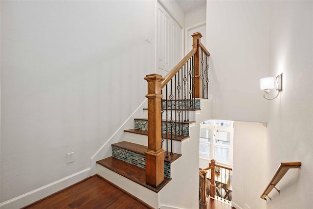 stairs featuring a towering ceiling, baseboards, and wood finished floors