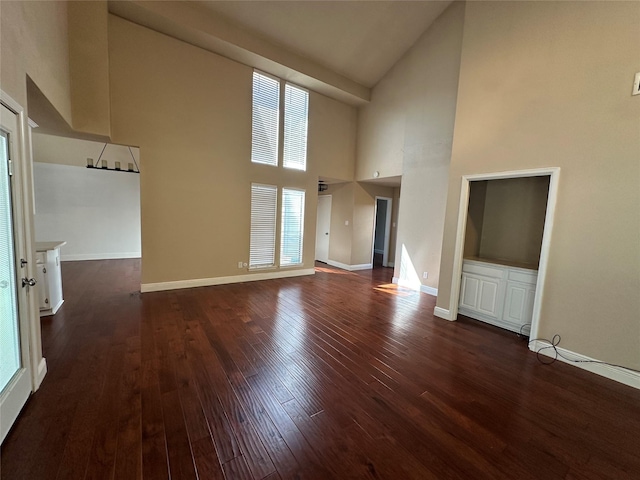 unfurnished living room with dark wood finished floors, high vaulted ceiling, and baseboards