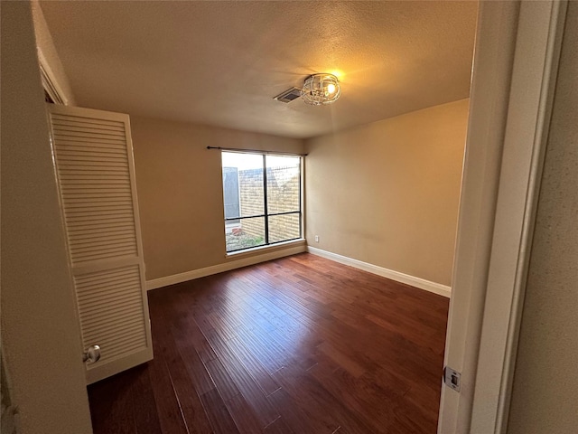 unfurnished bedroom with visible vents, baseboards, a textured ceiling, and dark wood-style floors