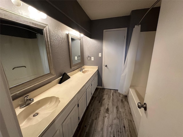 full bathroom with double vanity, wood finished floors, a textured wall, and a sink