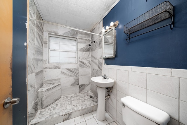 bathroom with toilet, a tile shower, tile walls, and tile patterned floors